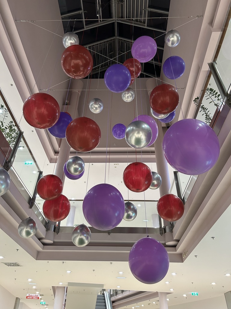 Große hängende Ballonkugeln in Rot, Lila und Silber in einem mehrstöckigen Innenraum