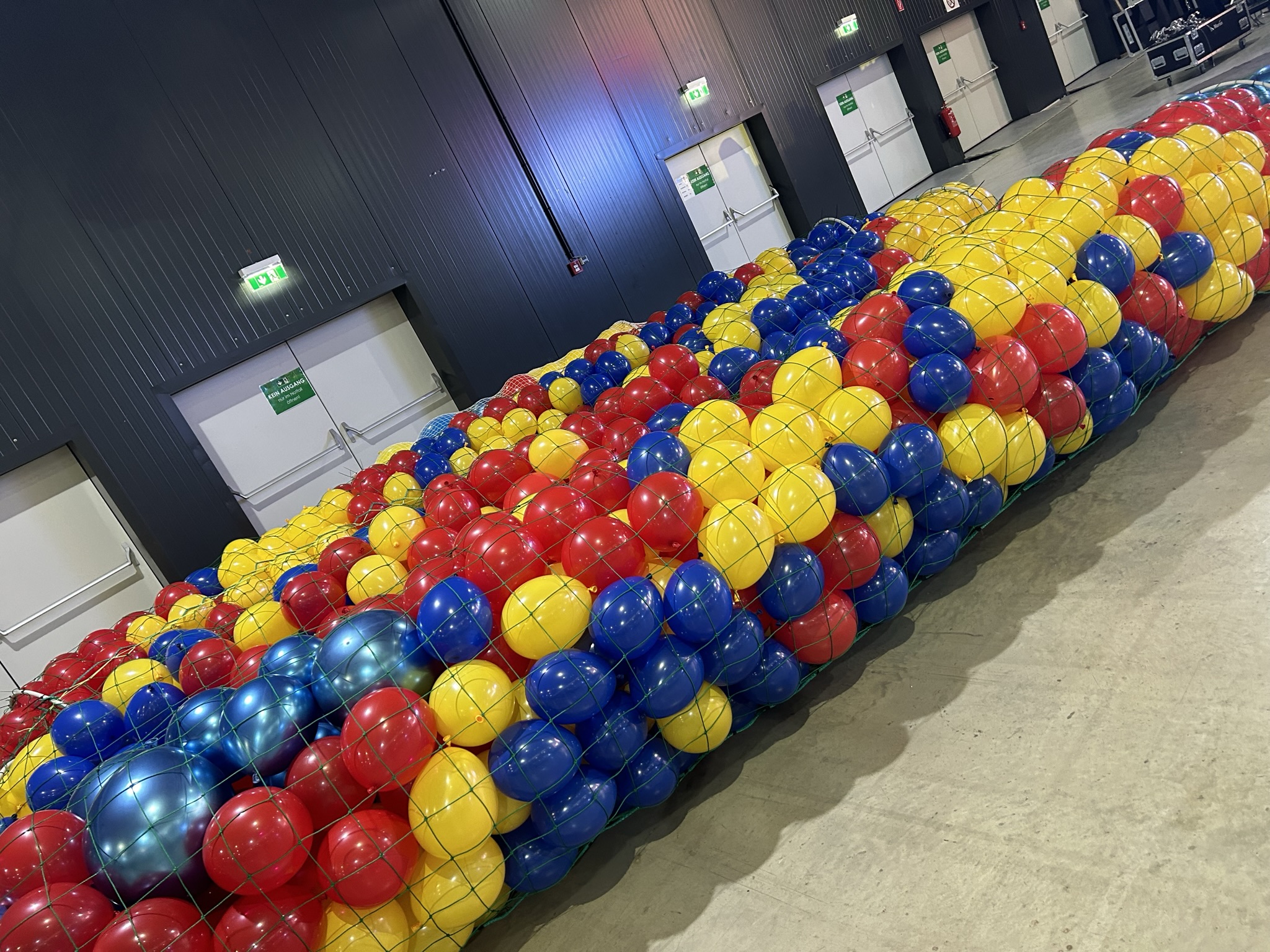 Große Ballonfüllung in Rot, Gelb und Blau innerhalb einer Gitterkonstruktion in einer Halle