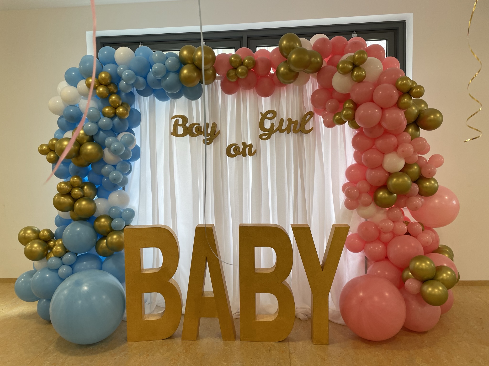 Gender-Reveal-Setup mit rosa-blauem Ballonbogen, goldenen Details und großen BABY-Buchstaben