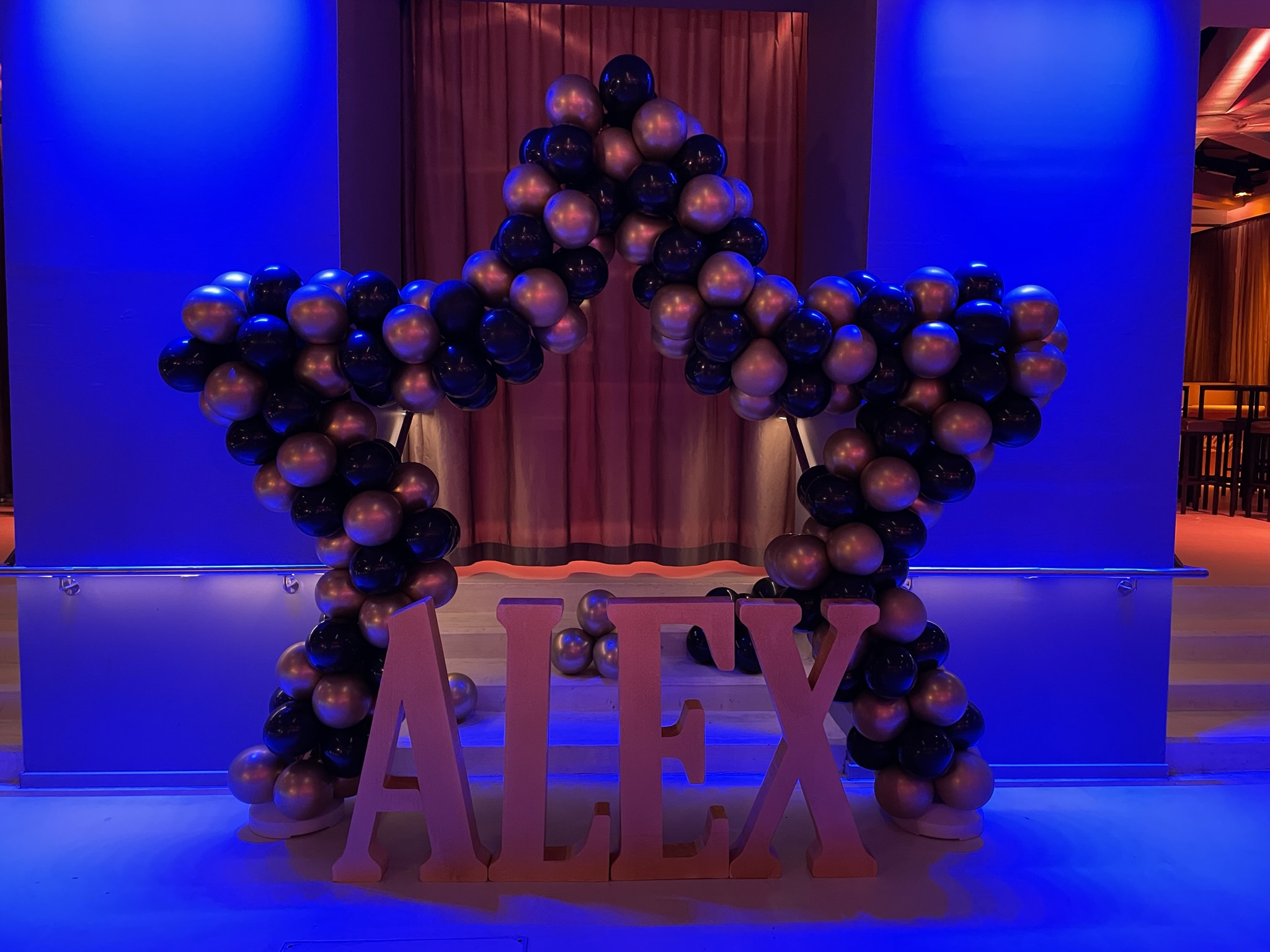 Dunkles Eventsetup mit blau-schwarzer Balloninstallation und großen Namensbuchstaben